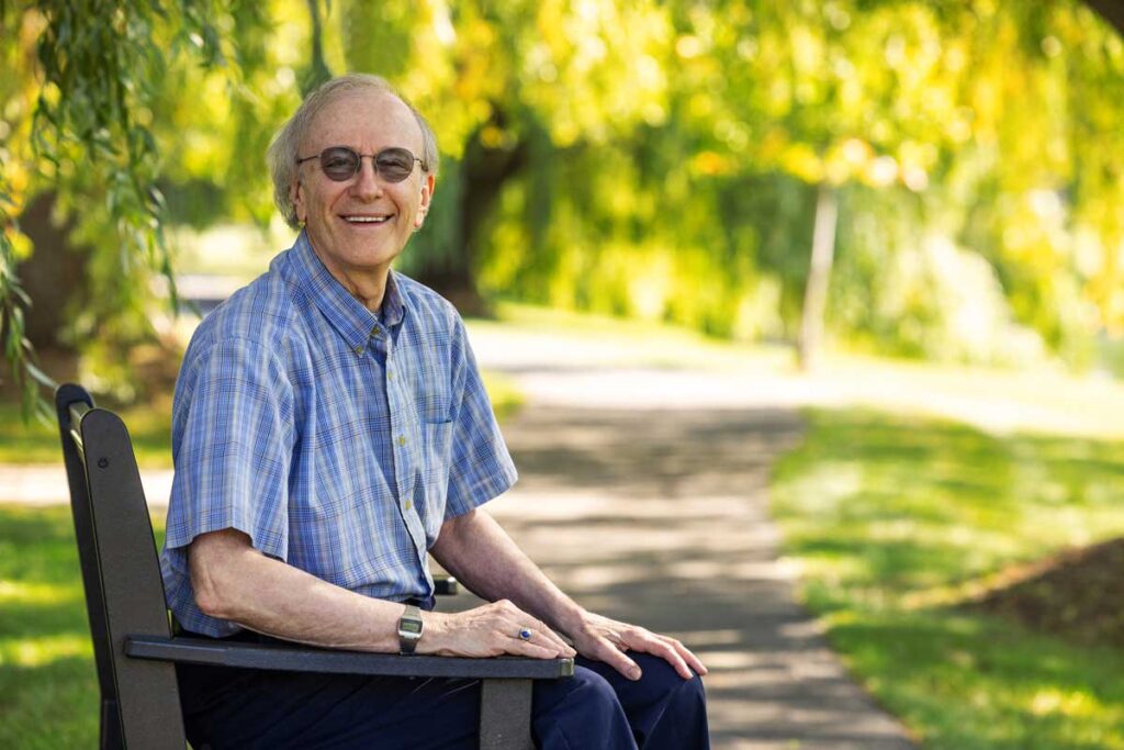 Smiling old man sits on bench in park.