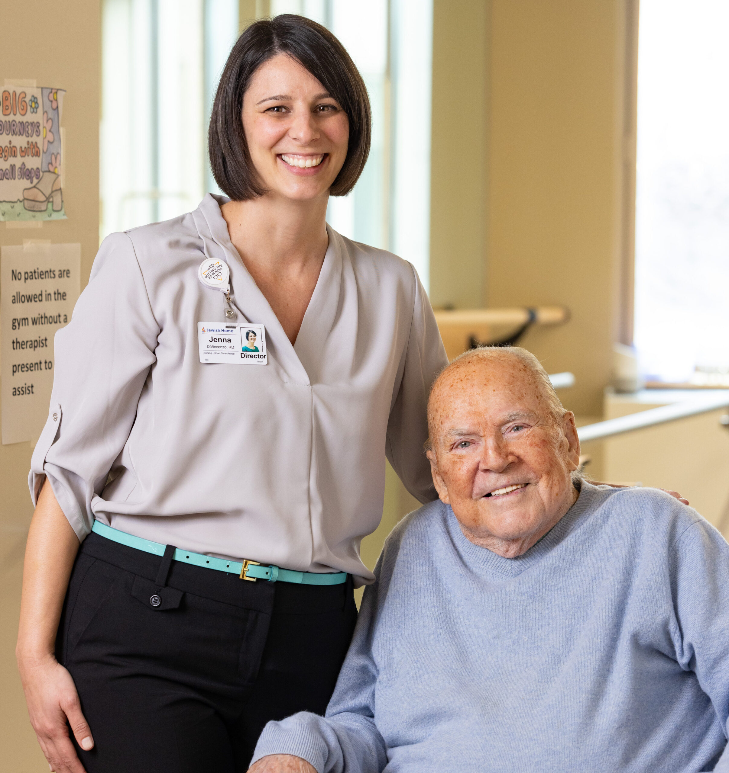 Nursing staff stands next to a seated patient, both smiling.